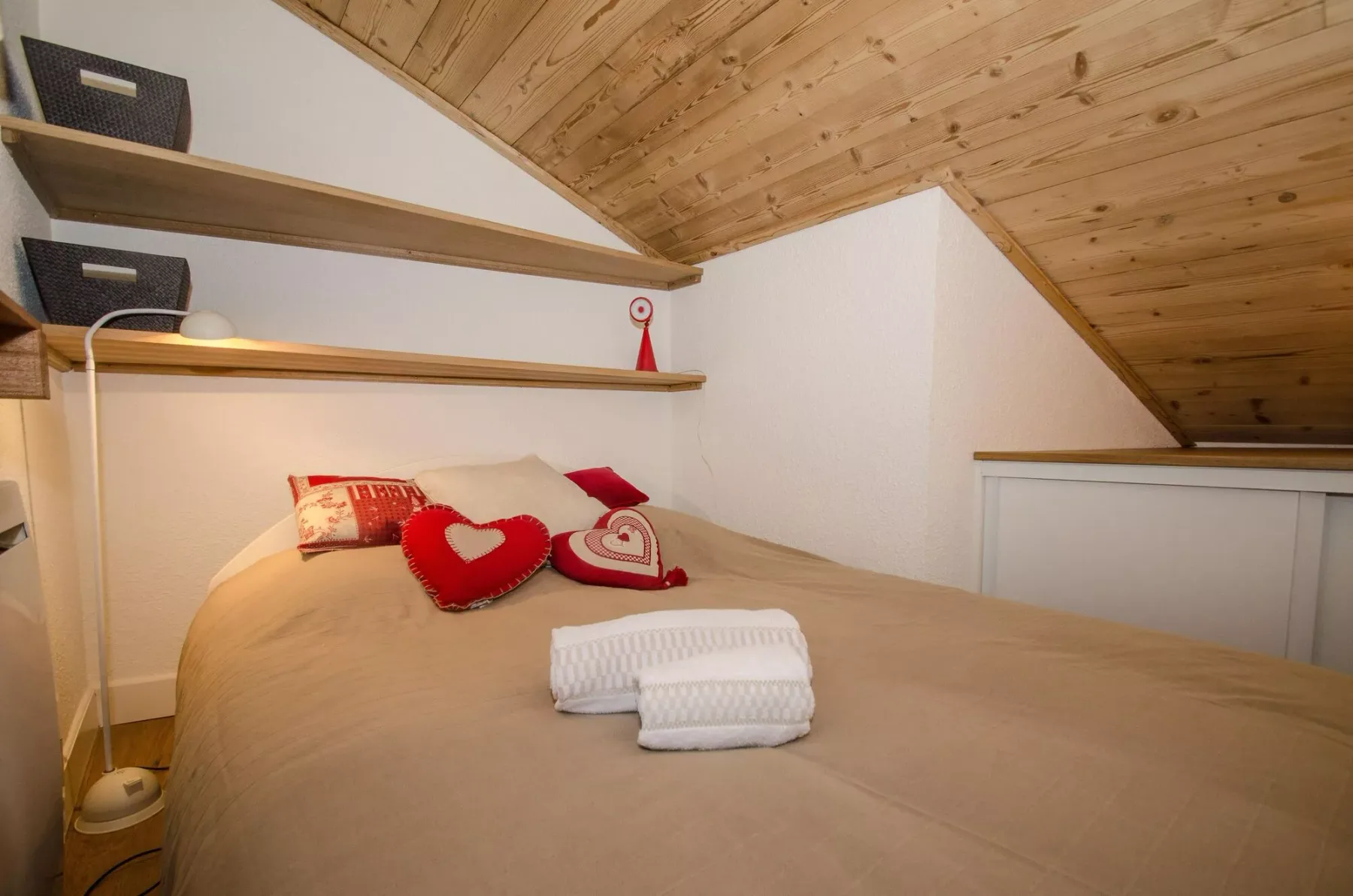 A bedroom with a bed beneath a sloped wooden ceiling.