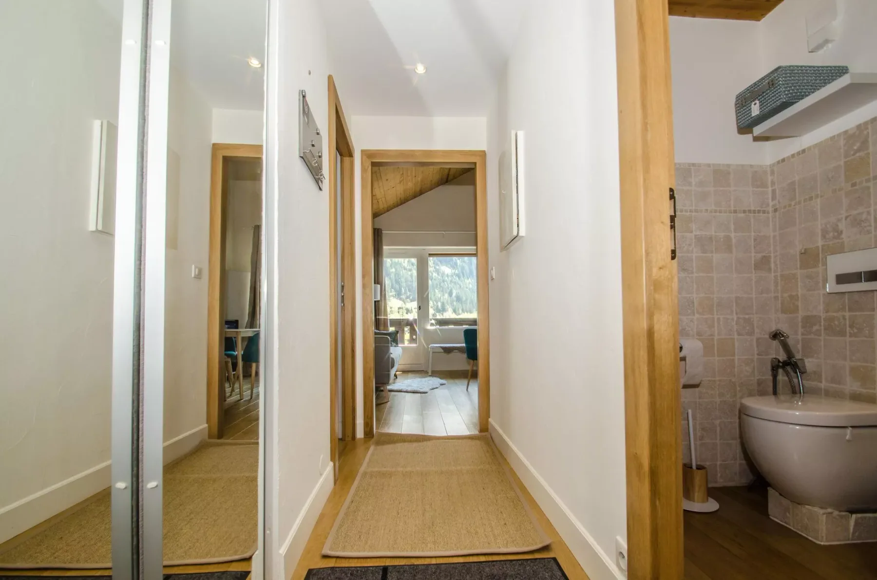 A hallway leads to a bright room, with a tiled bathroom visible through an open doorway.