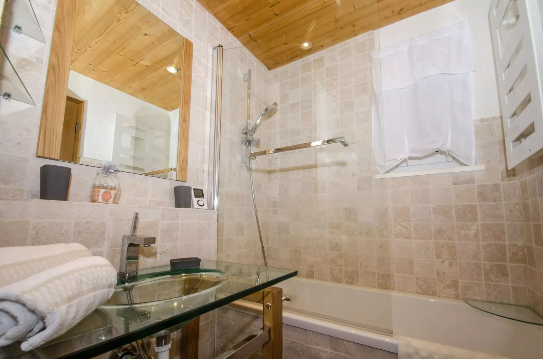 A tiled bathroom with a bathtub, shower, and glass vanity.