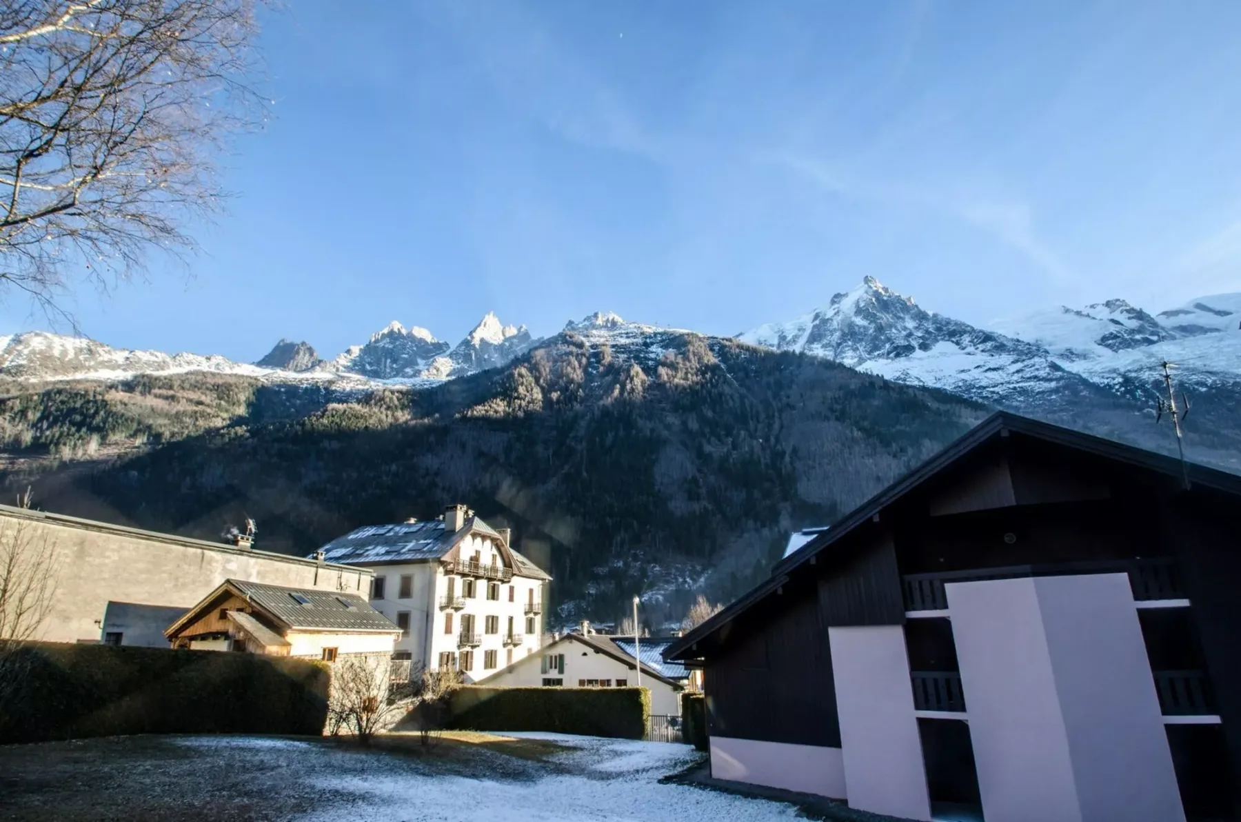 Snow-dusted buildings sit beneath a mountain range on a clear day.