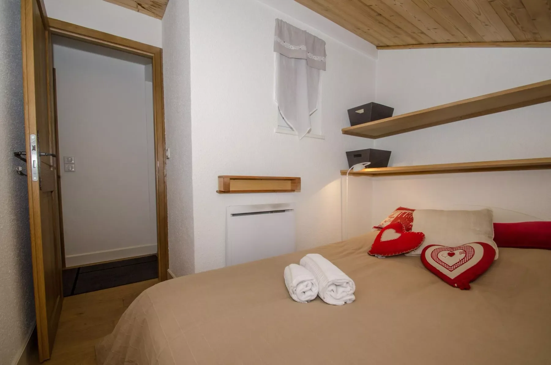 A bedroom with a bed, heart-shaped pillows, and a wooden ceiling.