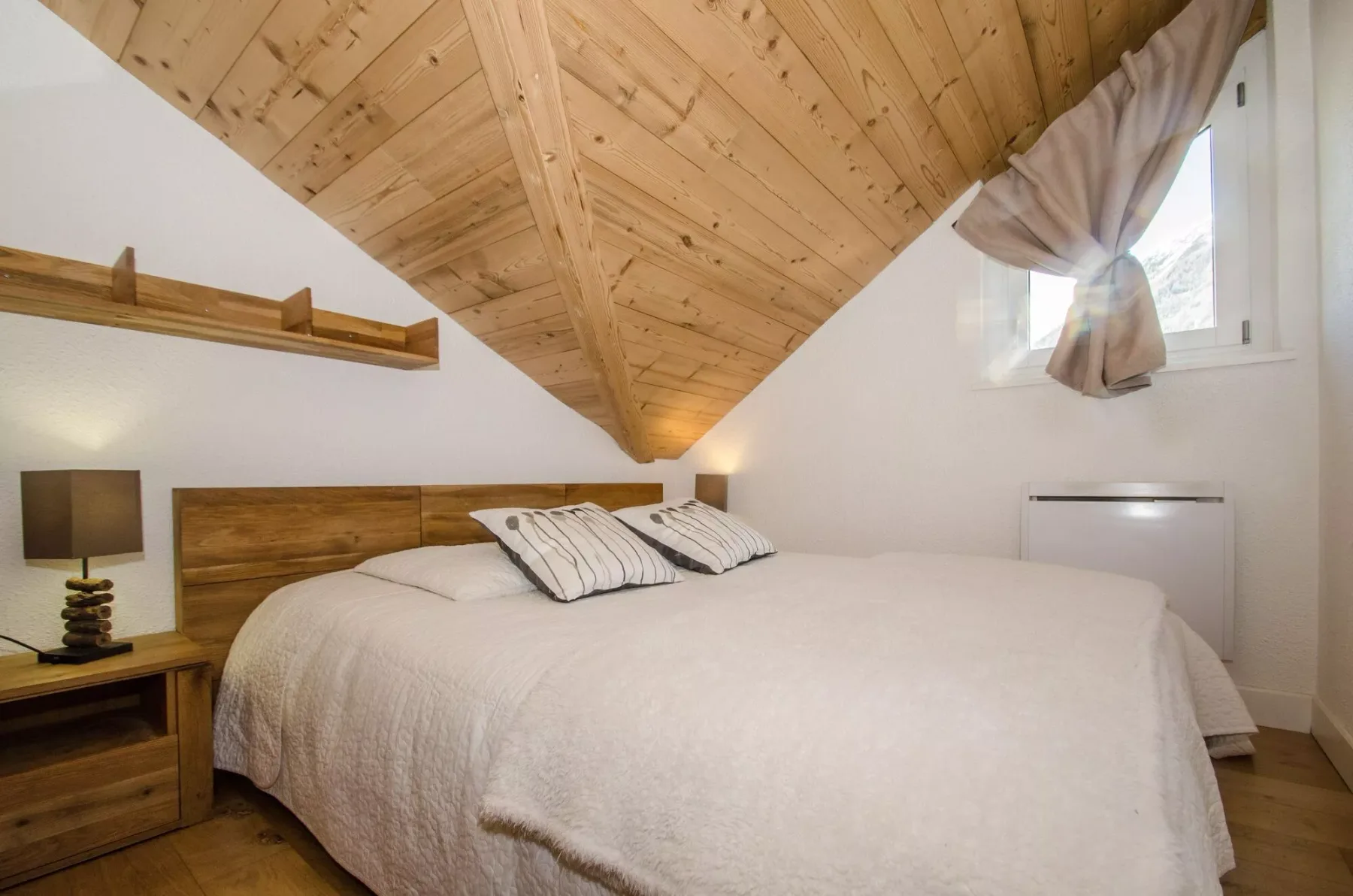 A bedroom with a large bed beneath a sloped wooden ceiling.