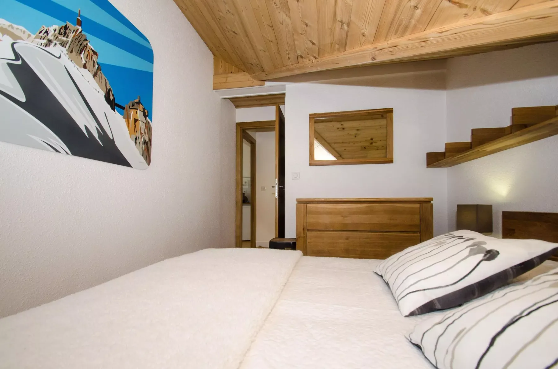 A bedroom with a bed, wooden ceiling, and a staircase along the wall.