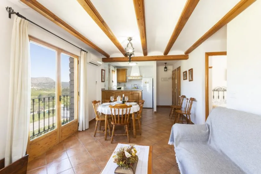 A bright dining and living area with exposed ceiling beams and a table by the windows.