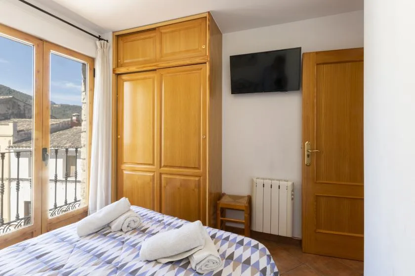 A bedroom with a patterned bedspread, wooden wardrobe, and windows overlooking a balcony.