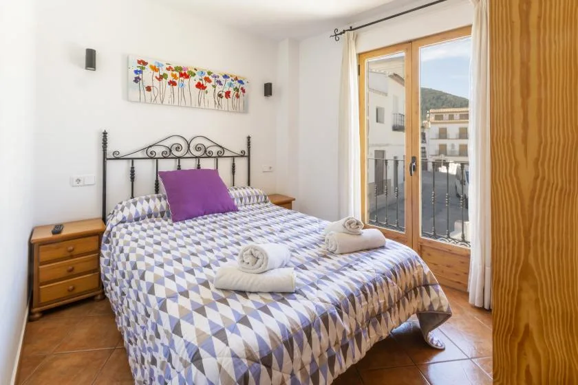 A bedroom with a patterned bedspread, bedside tables, and glass doors opening to a balcony.