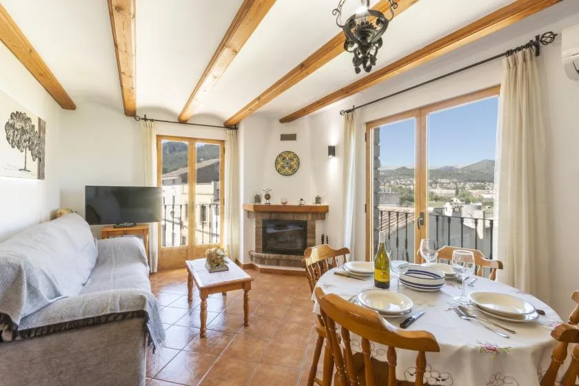 A bright living and dining room opens onto a balcony with views of the surrounding hills.
