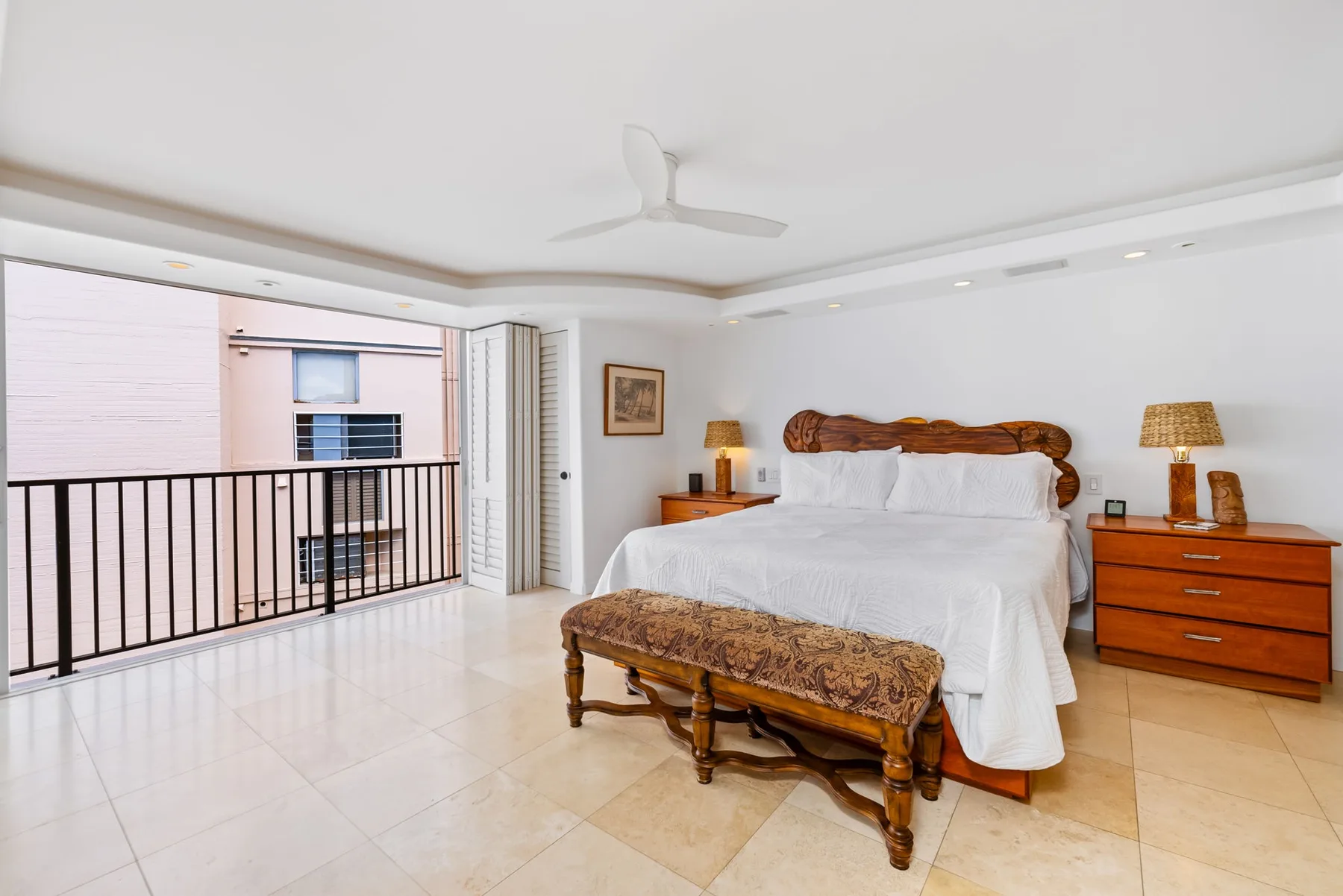 Un dormitorio con una cama, un banco y una cómoda junto a una barandilla de balcón.