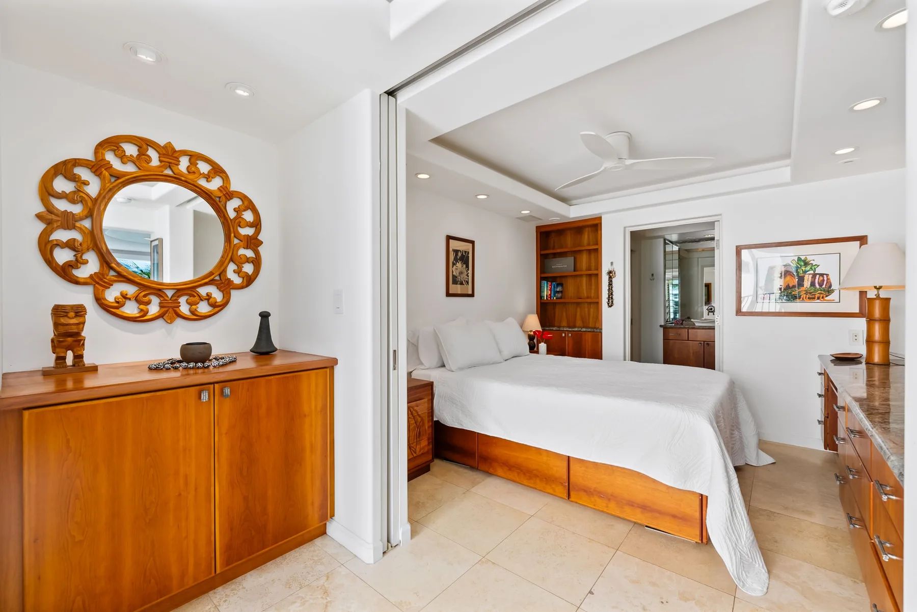 Un dormitorio luminoso con una cama blanca, muebles de madera y un espejo ornamentado.