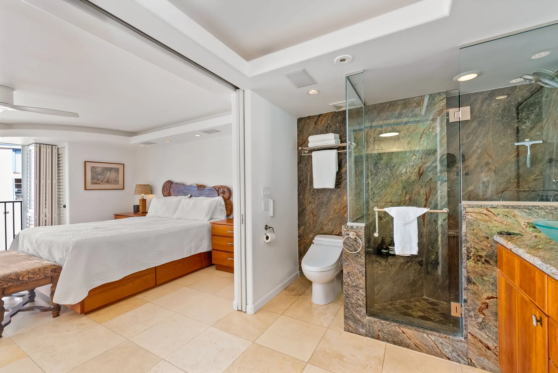 Un dormitorio se abre a un baño con una ducha de vidrio.