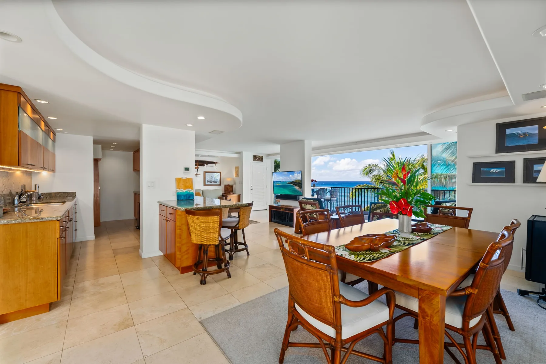 Una zona abierta de comedor y cocina con una mesa de madera junto a grandes ventanales.