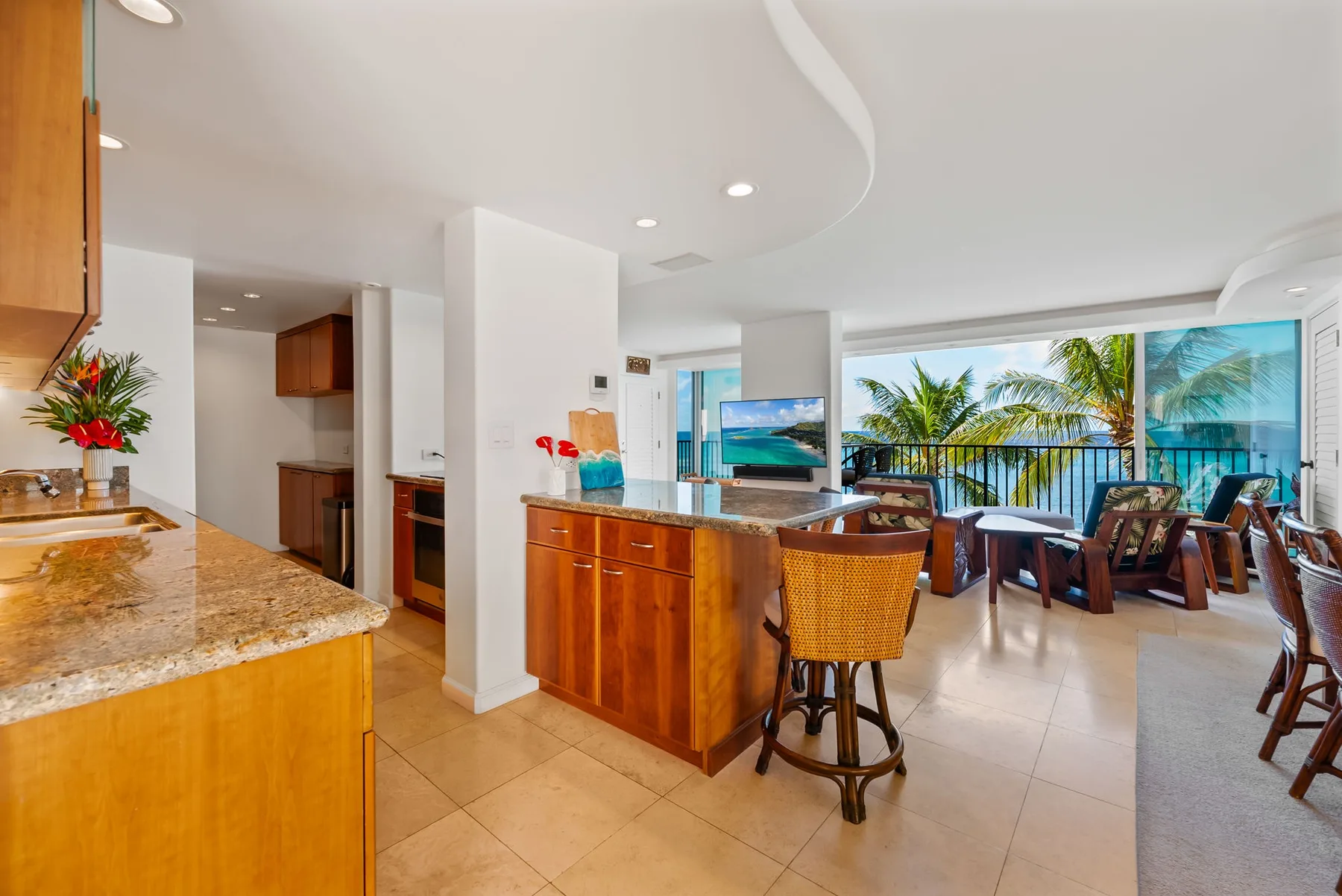Una cocina y comedor de planta abierta dan a un balcón con vistas tropicales.