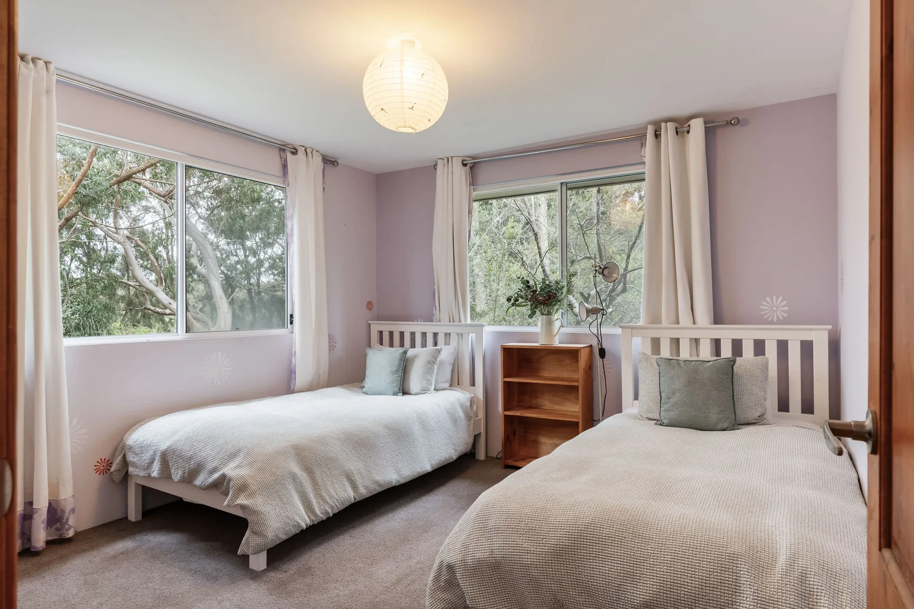 Dormitorio con dos camas junto a grandes ventanas con vistas a los árboles.