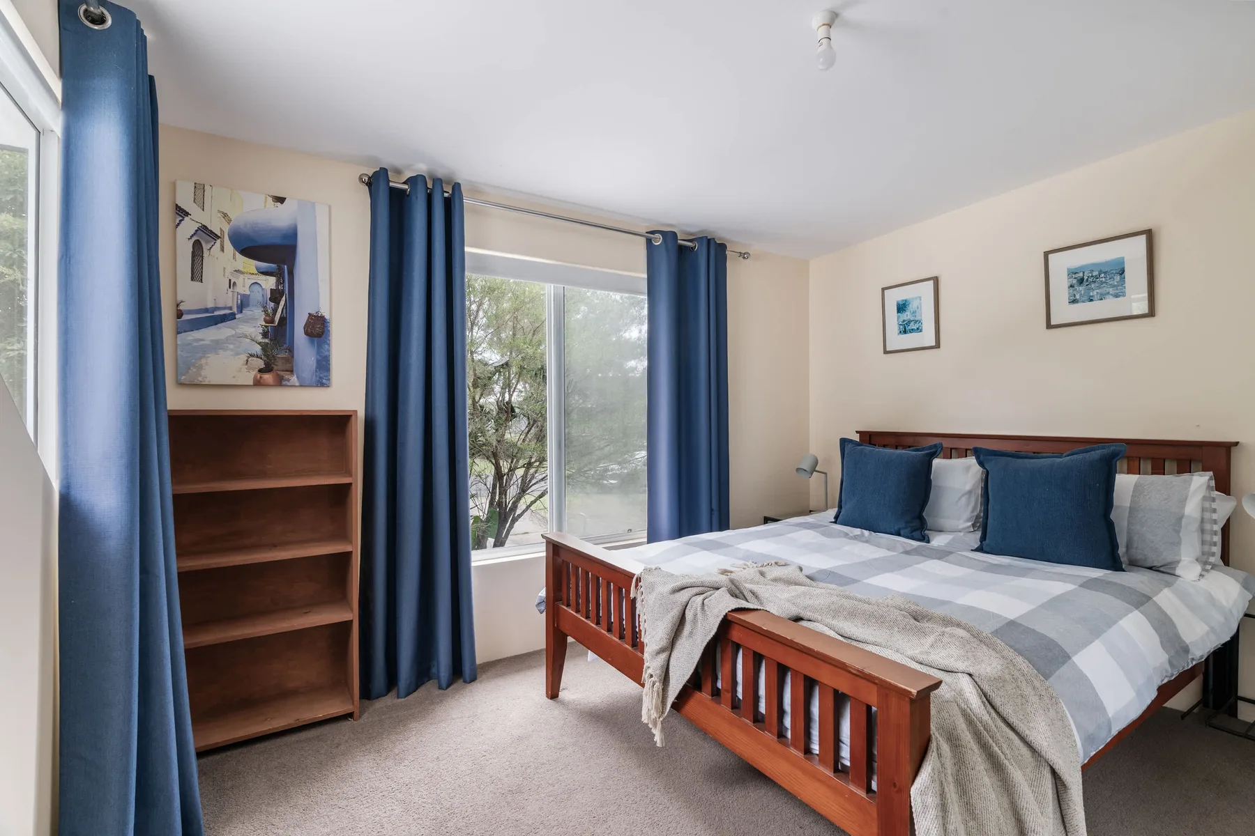 Un dormitorio con una cama de madera, cortinas azules y una estantería alta.