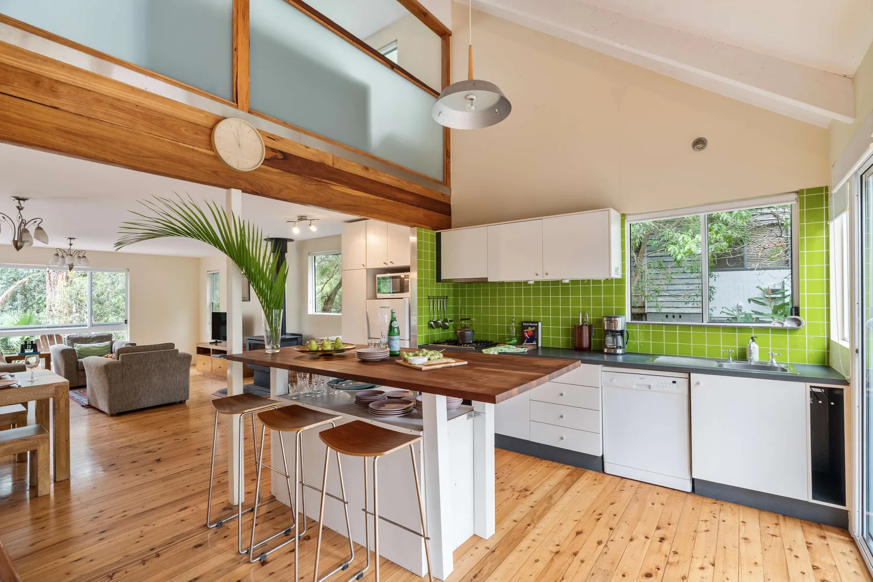 Cocina y comedor de planta abierta con isla de madera y azulejos verdes.
