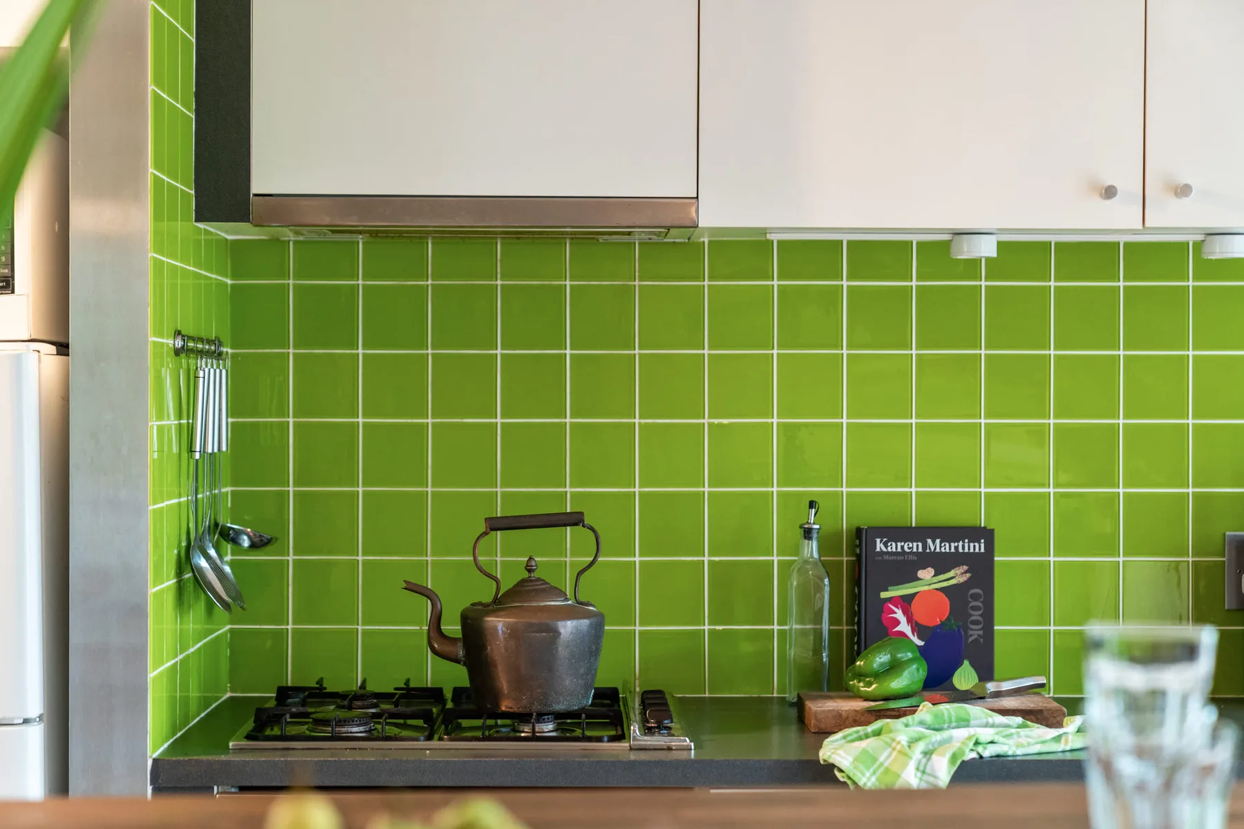 Una cocina con una estufa de gas frente a un llamativo salpicadero de azulejos verdes.