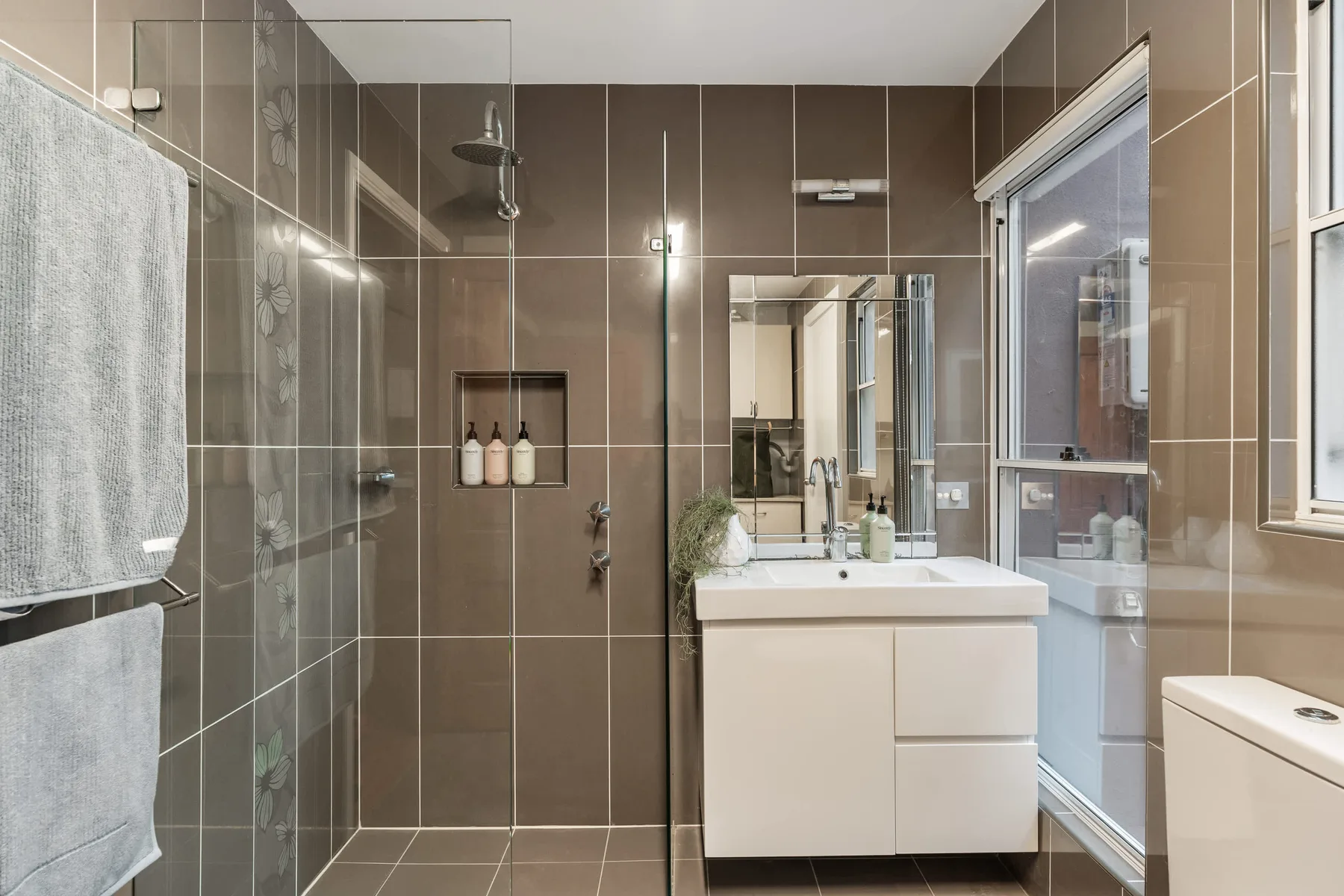 Baño alicatado con ducha, lavabo y una ventana grande.