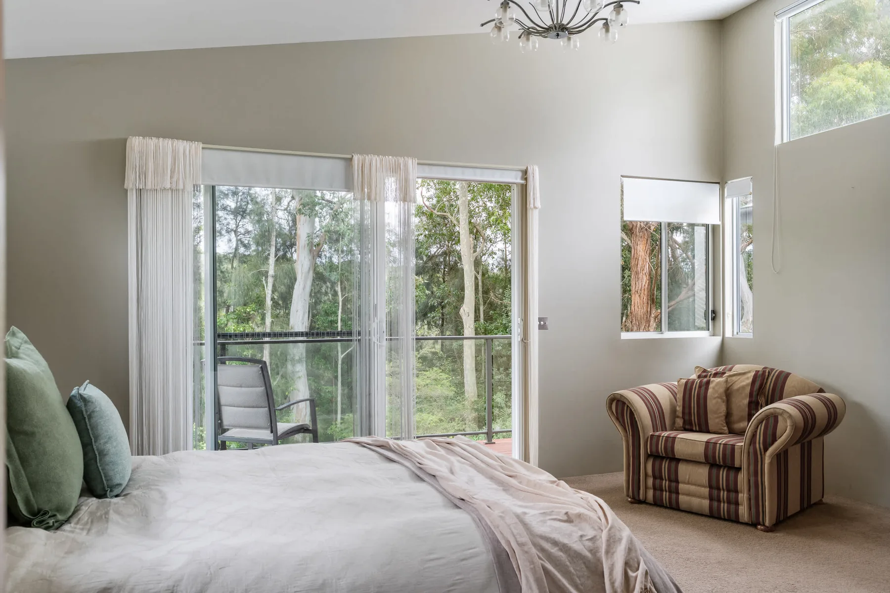 Un dormitorio luminoso con una cama grande y ventanas con vistas a los árboles.