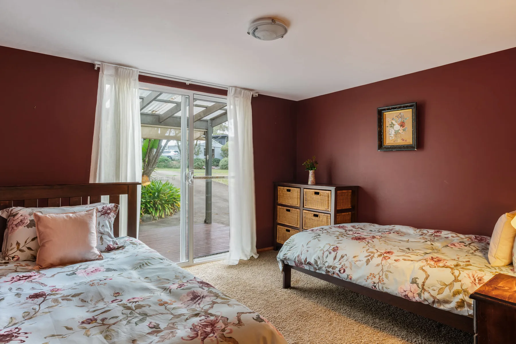 Un dormitorio con dos camas, ropa de cama floral y puertas corredizas de vidrio que dan a un patio.