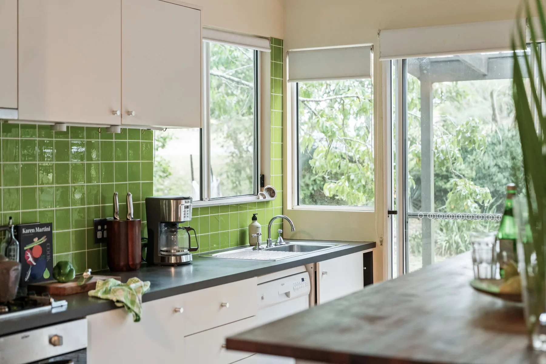 Una cocina luminosa con paredes de azulejos verdes y un fregadero sobre la encimera.