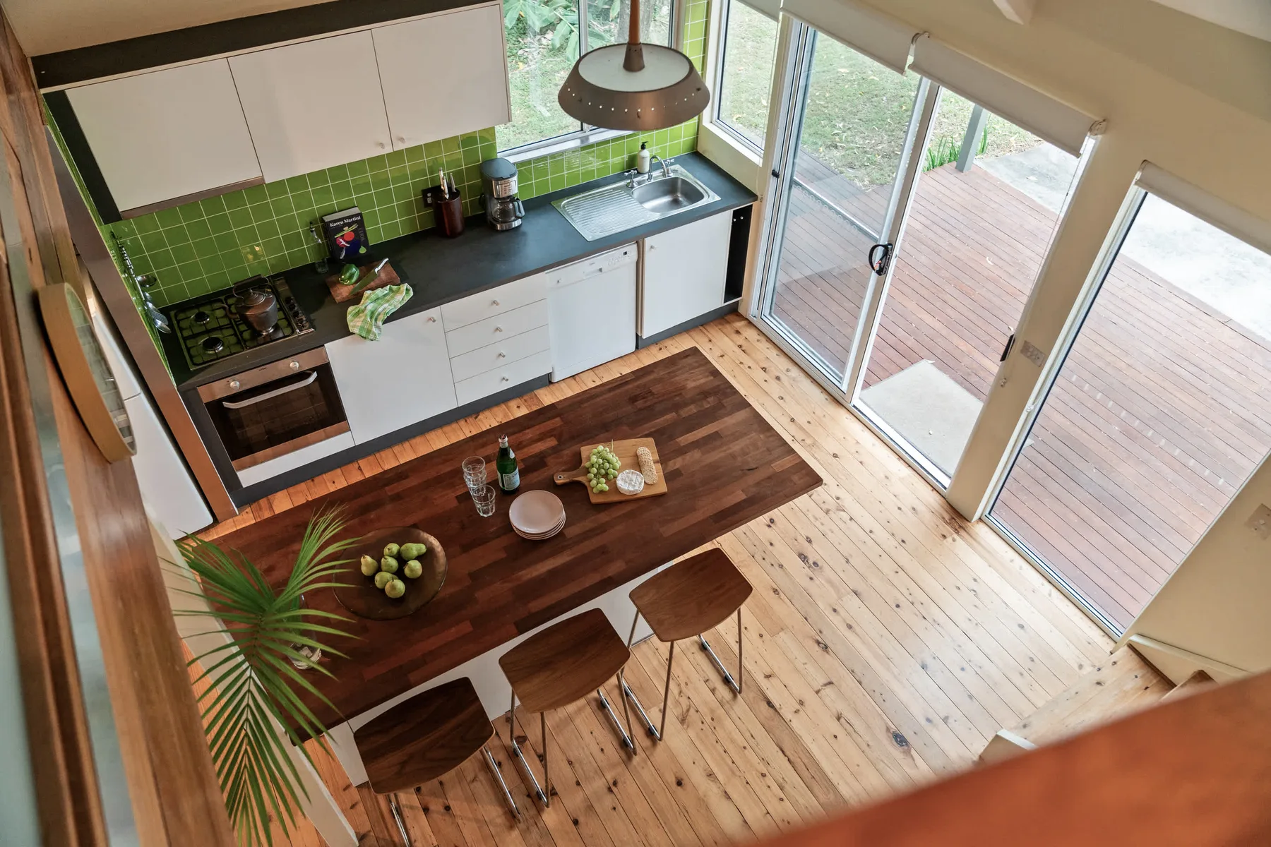 Una cocina luminosa con zona de comedor, azulejos verdes y puertas de vidrio hacia una terraza.