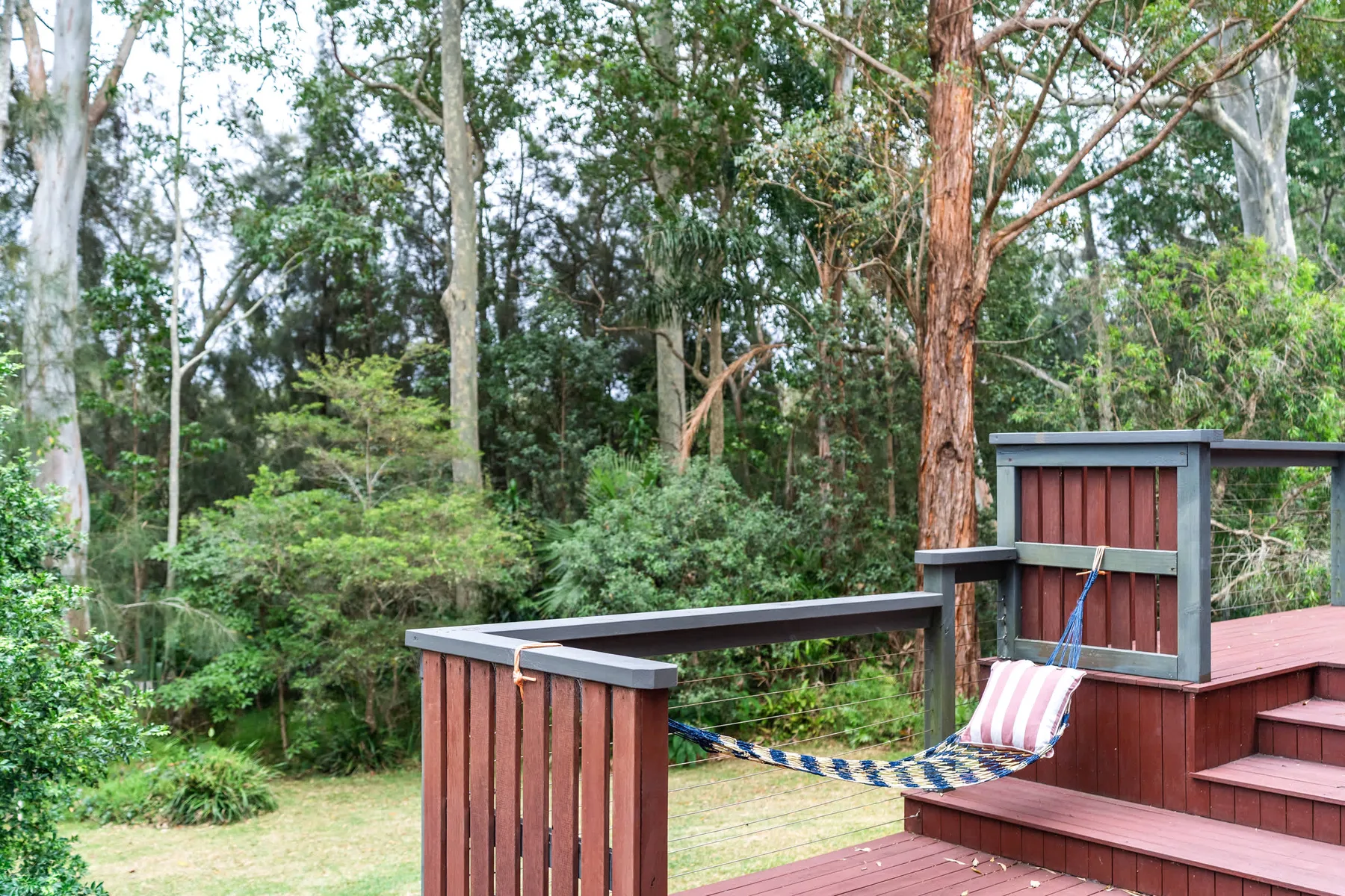 Una terraza de madera con una hamaca a rayas está rodeada de árboles y vegetación.