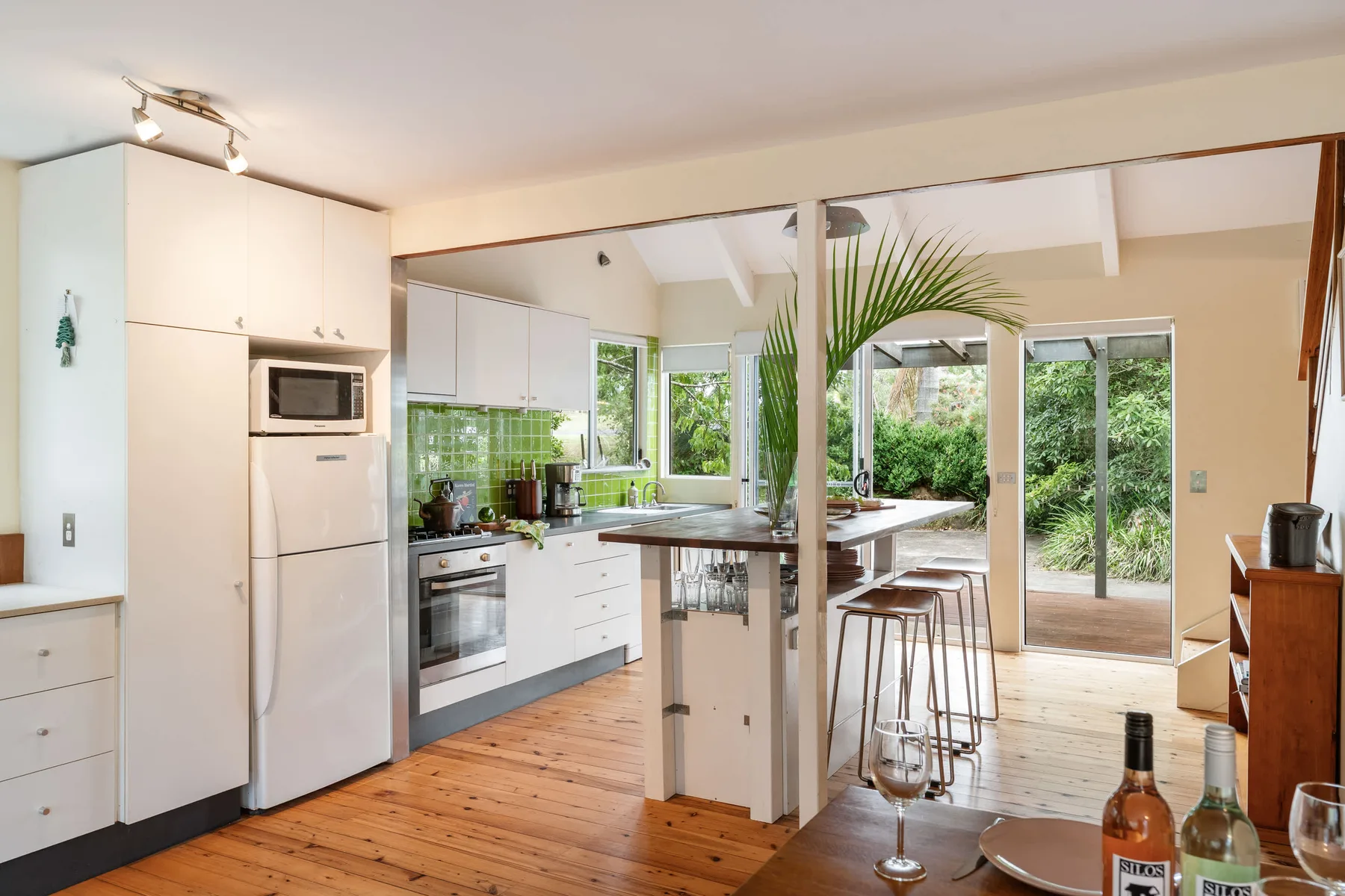 Cocina y comedor de planta abierta con una barra, taburetes y vistas al jardín.