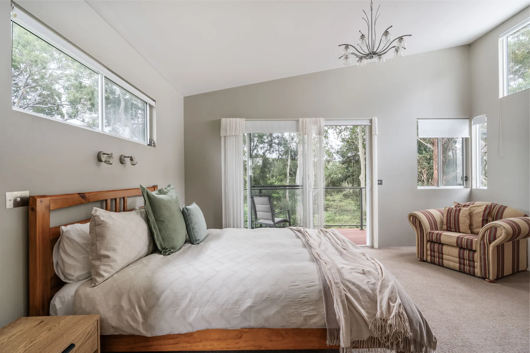 Un dormitorio luminoso con una cama junto a una puerta corrediza de vidrio y vegetación.