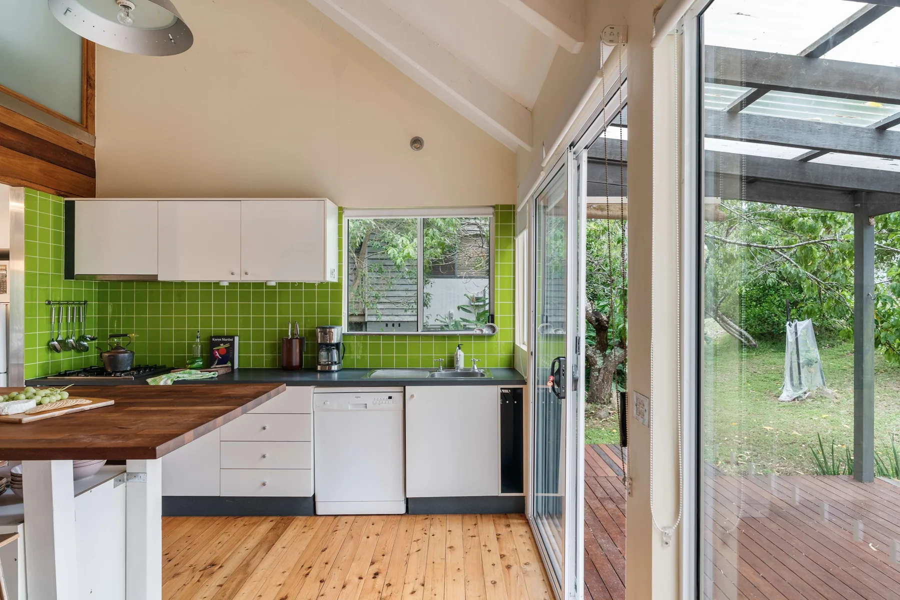Una cocina luminosa con paredes de azulejos verdes y grandes puertas de vidrio hacia una terraza.