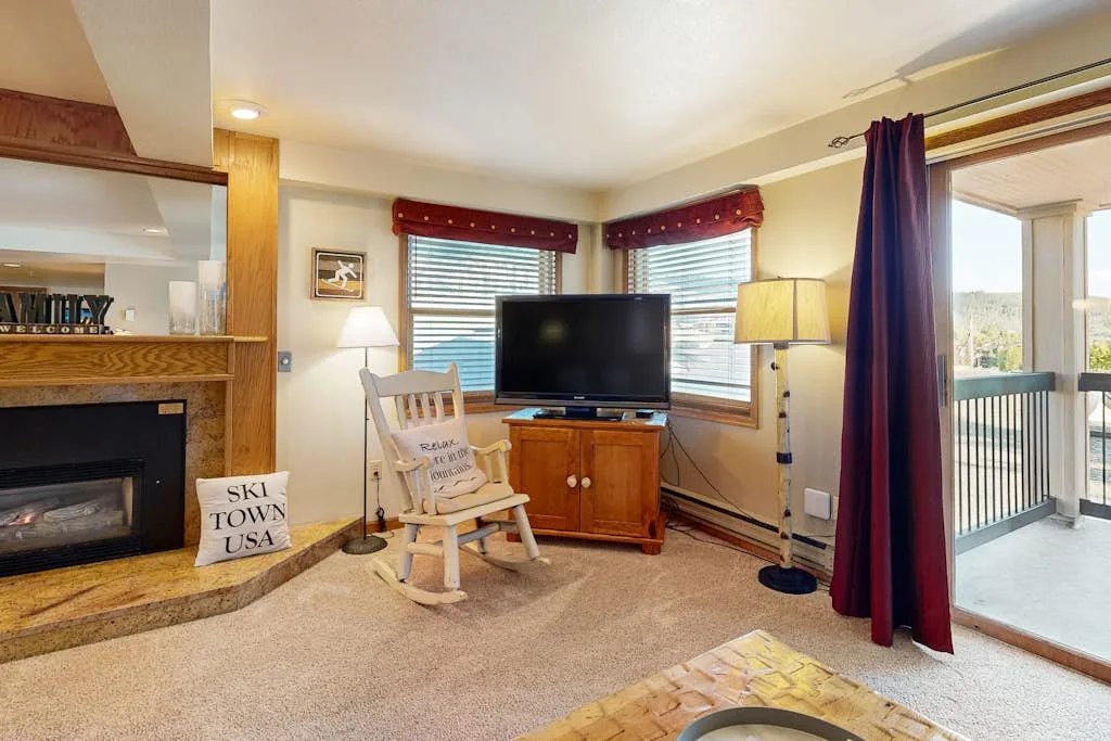 Una sala de estar con televisor, chimenea y puertas al balcón.