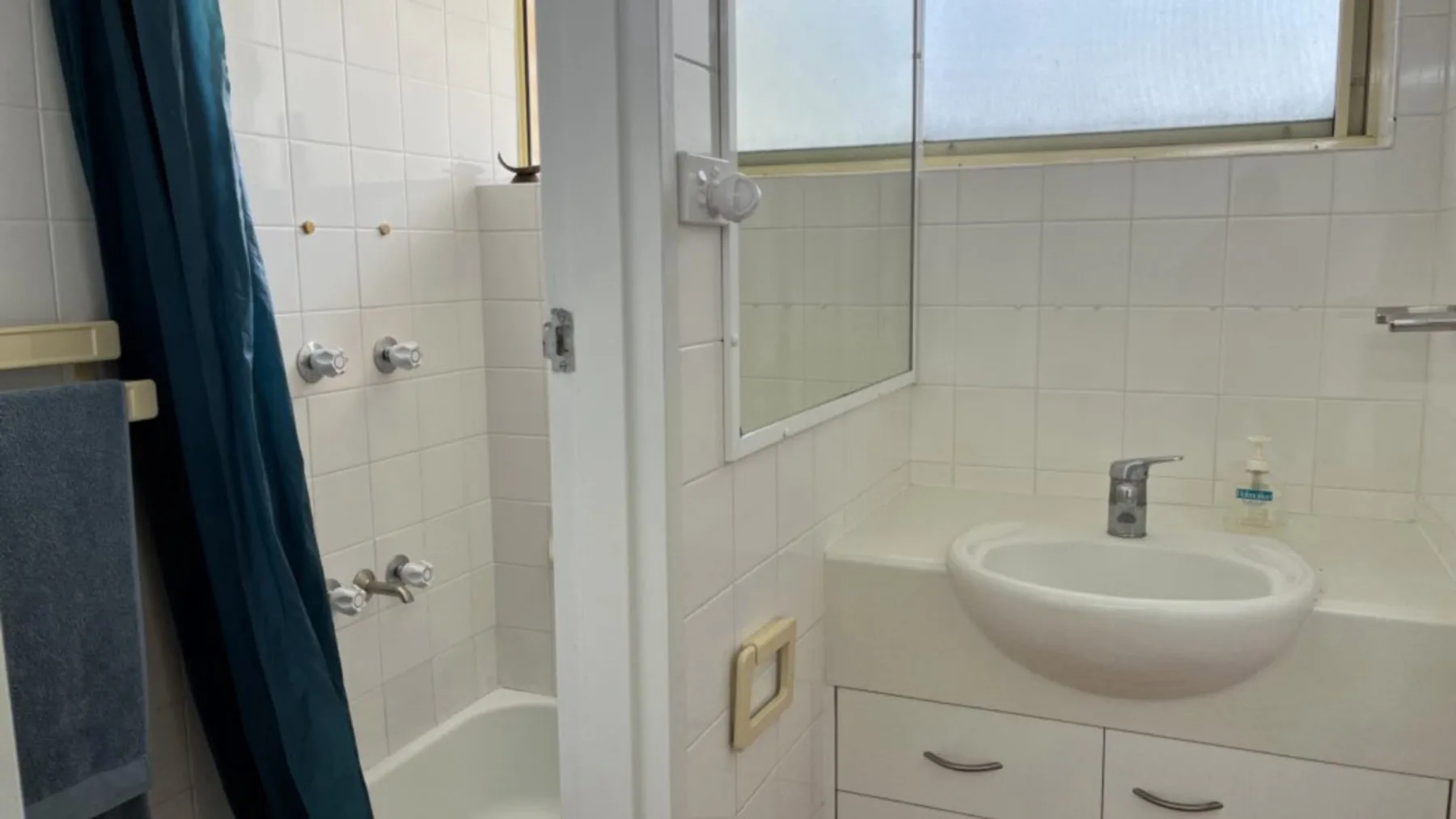A tiled bathroom with a bathtub, shower curtain, and sink beneath a window.