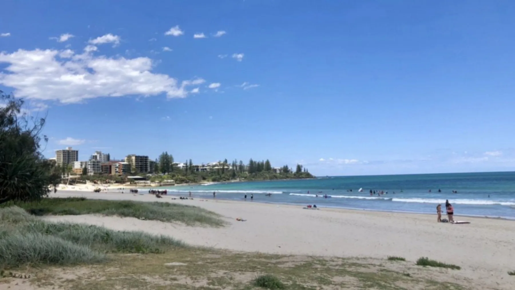 A sandy beach curves along calm blue water beneath a partly cloudy sky.