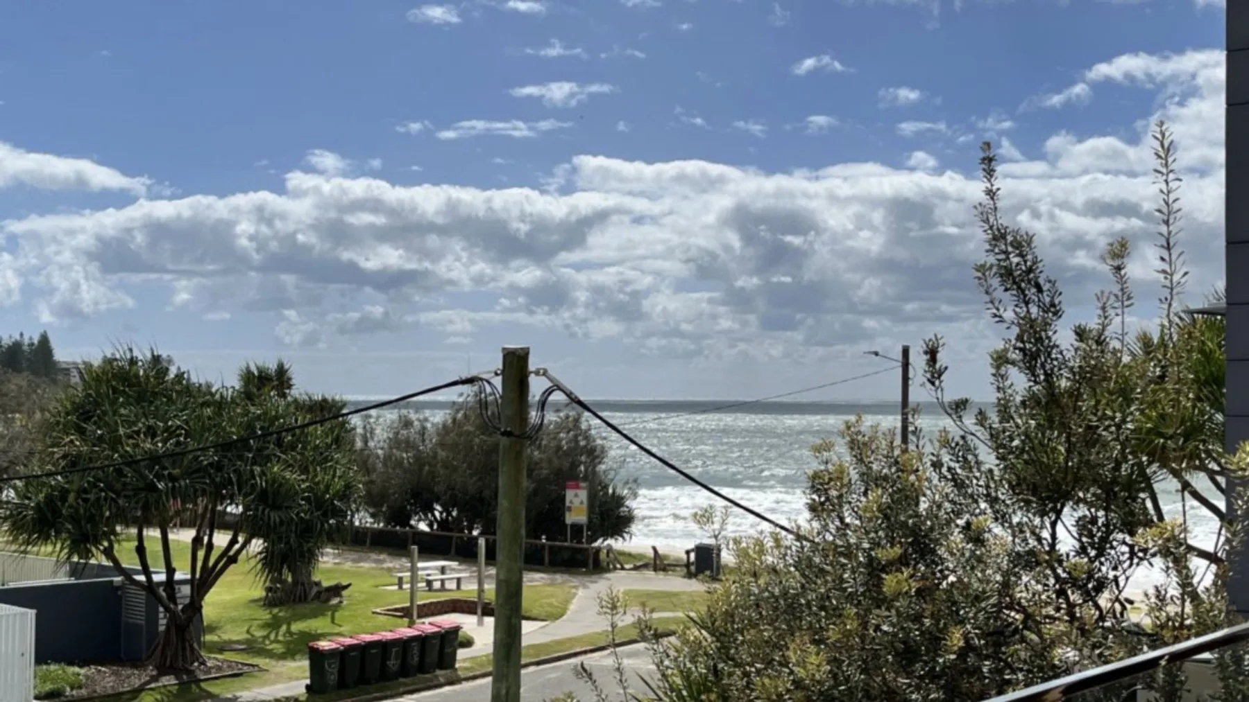 A coastal park with a path, trees, and ocean waves beyond.