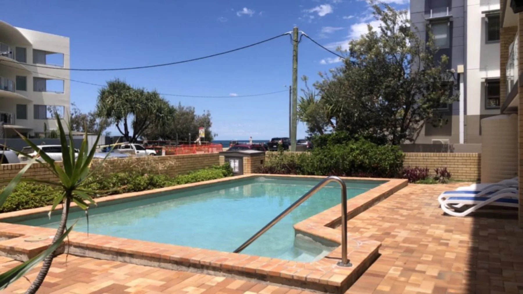 An outdoor swimming pool sits among paved patio areas and apartment buildings.