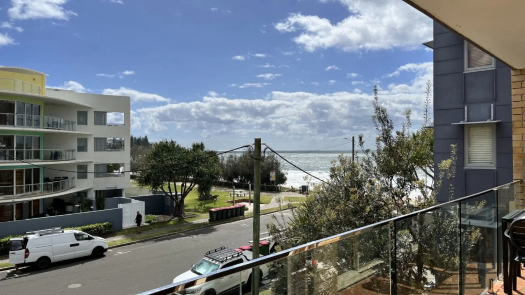 An apartment balcony overlooks a street, nearby buildings, and the ocean.