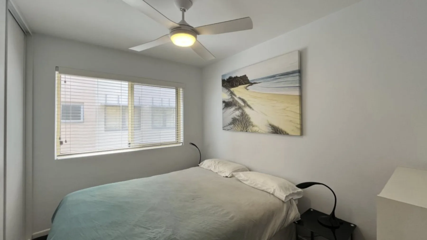 A bedroom with a bed, ceiling fan, and beach artwork on the wall.