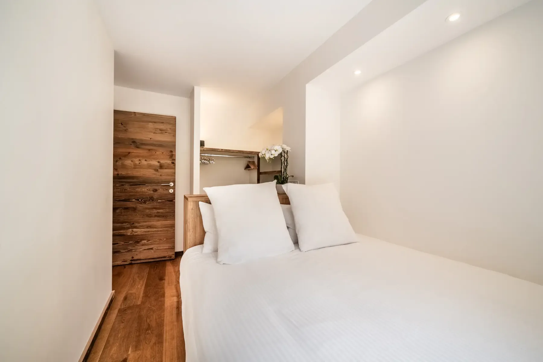 A bright bedroom with a bed, white bedding, and a wooden door.