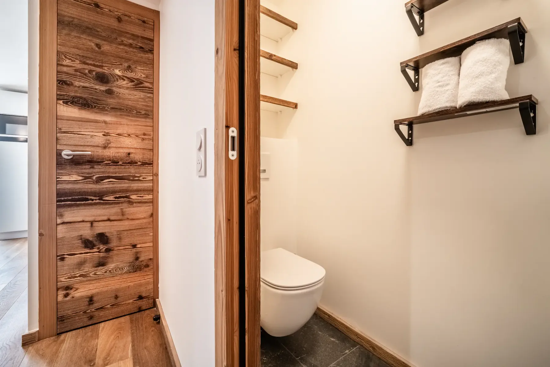 A small bathroom with a toilet and open shelves holding folded towels.