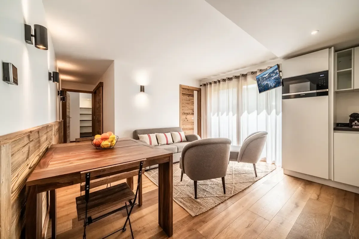 A bright dining and sitting area with a wooden table, seating, and a large window.