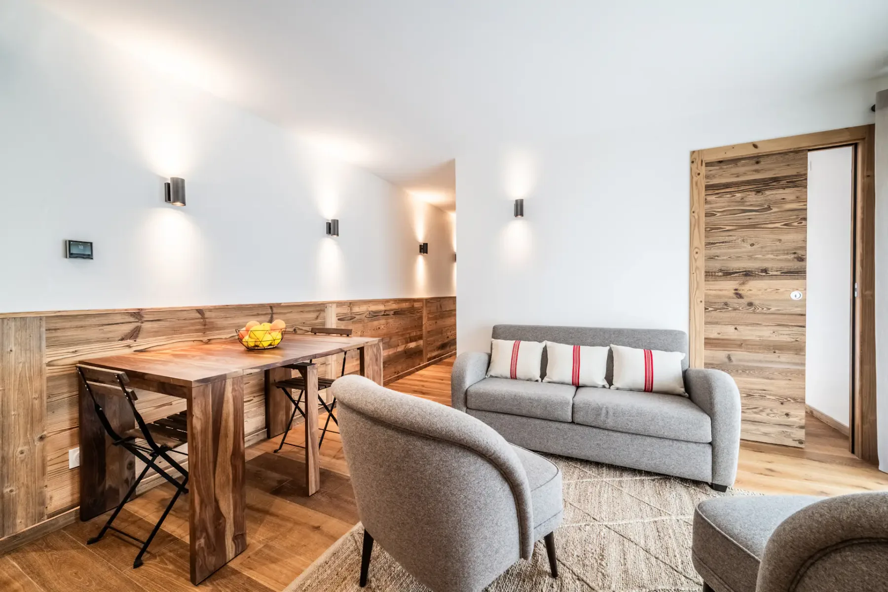 A bright living and dining area with a wooden table and gray seating.