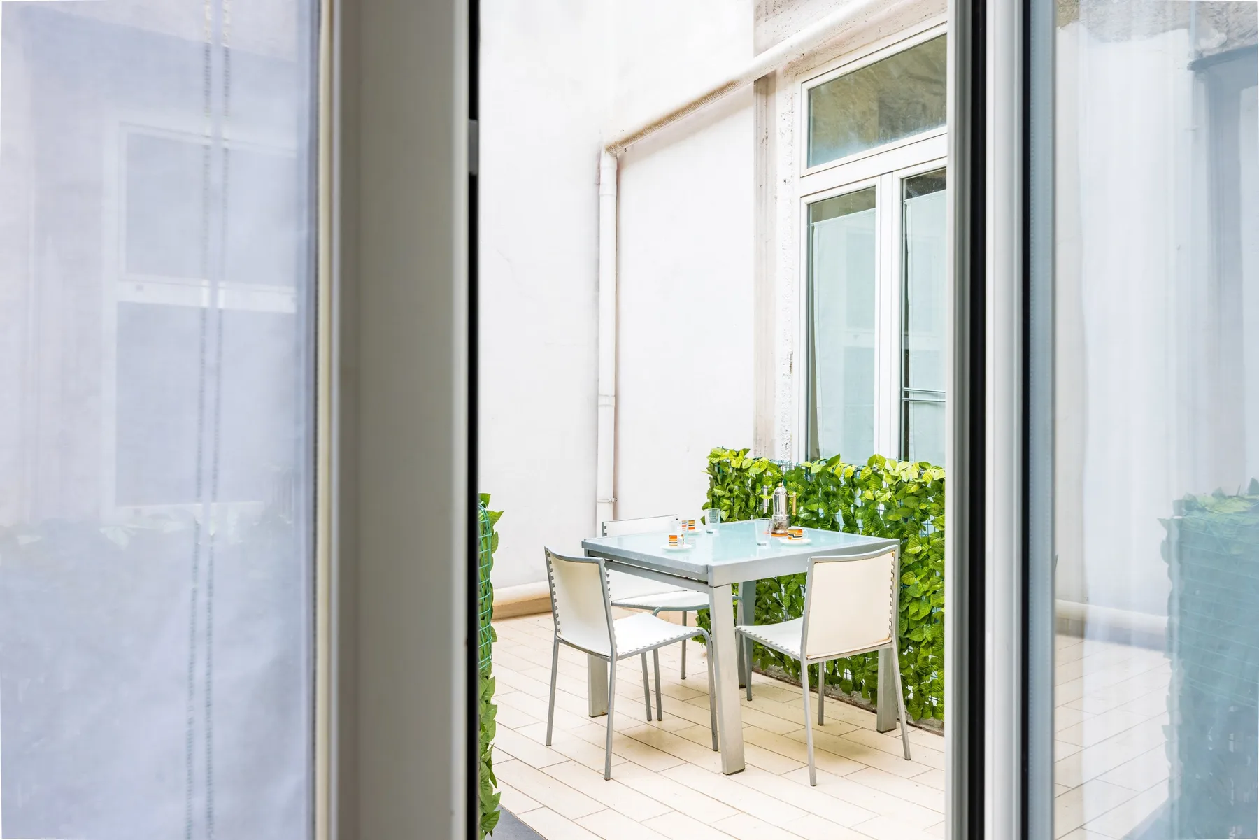 A small outdoor dining area with a table and chairs beside leafy plants.