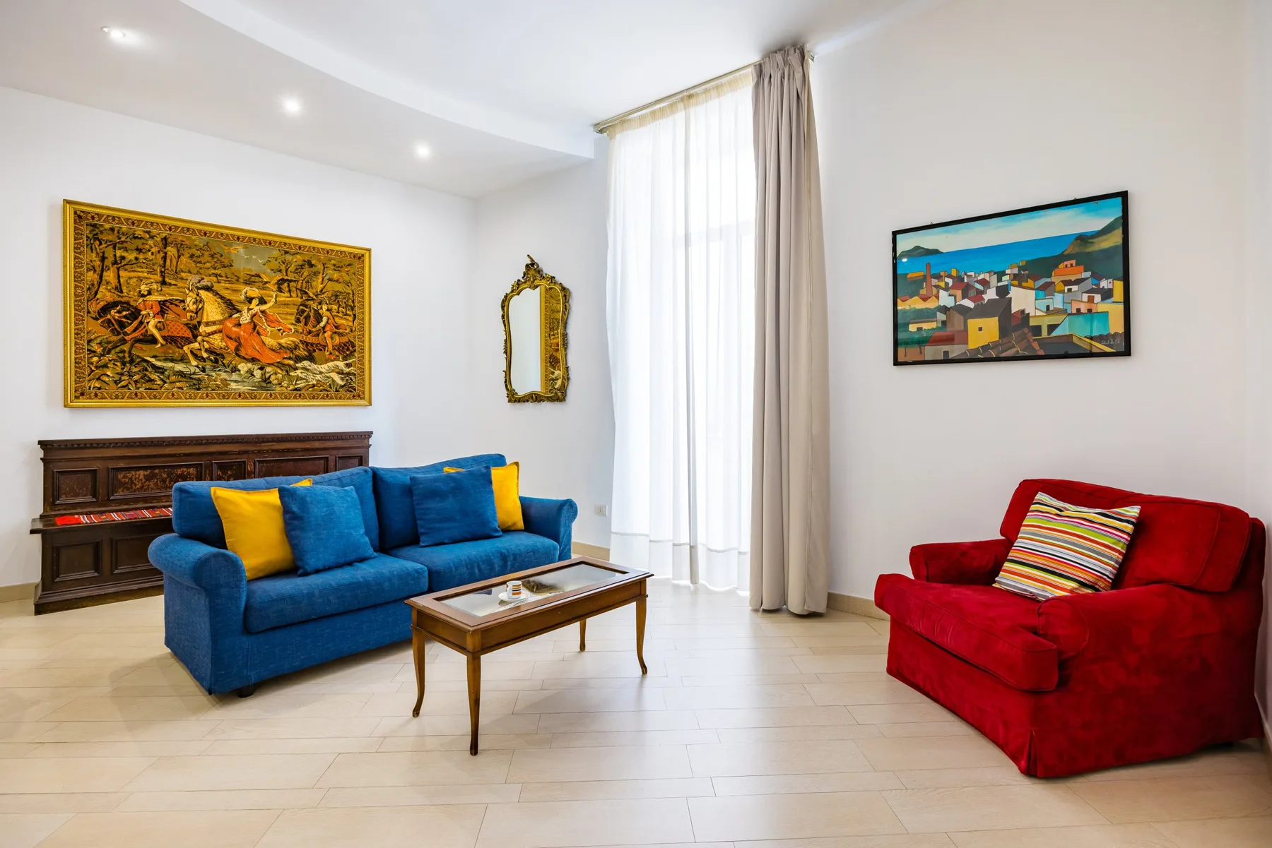 A living room with blue and red seating, a coffee table, and wall art.