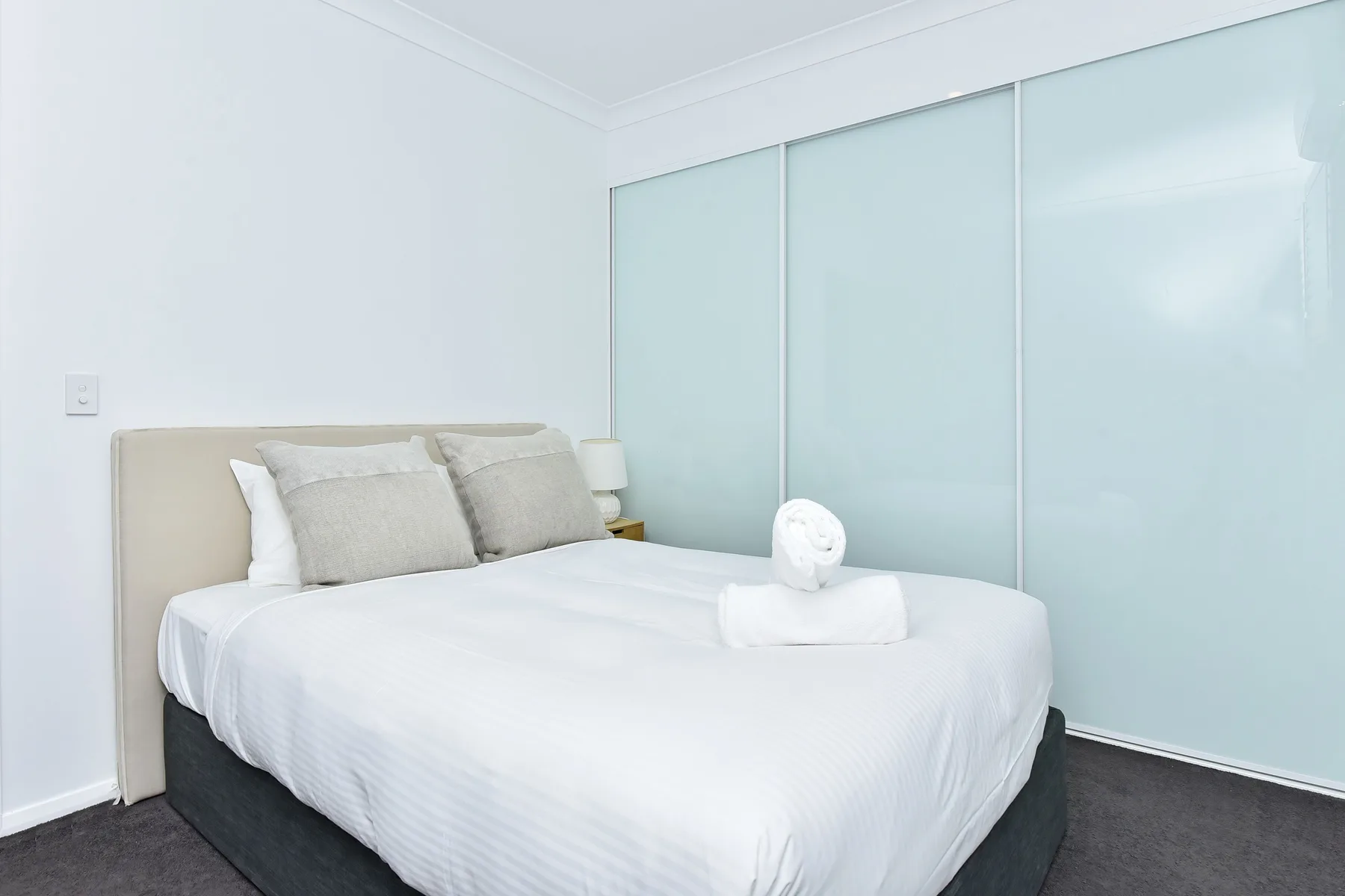 A bright bedroom with a neatly made bed and pale sliding panels.