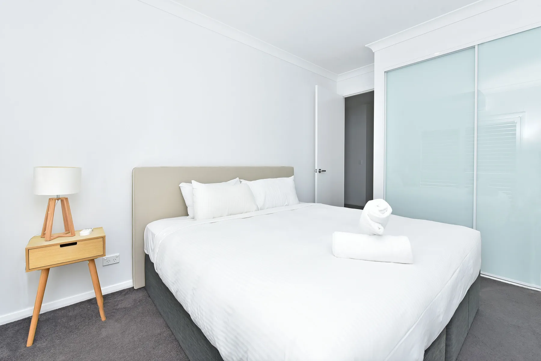 A bright bedroom with a neatly made bed and bedside table.