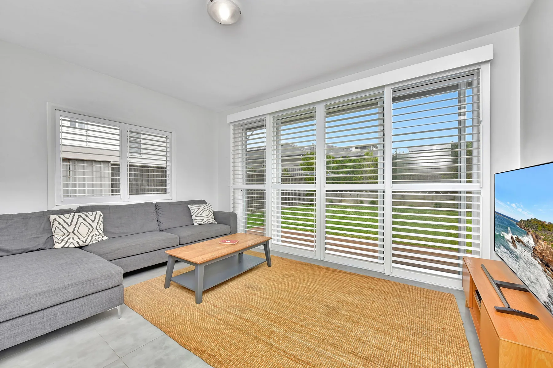 A bright living room with gray seating, a coffee table, and wide windows.