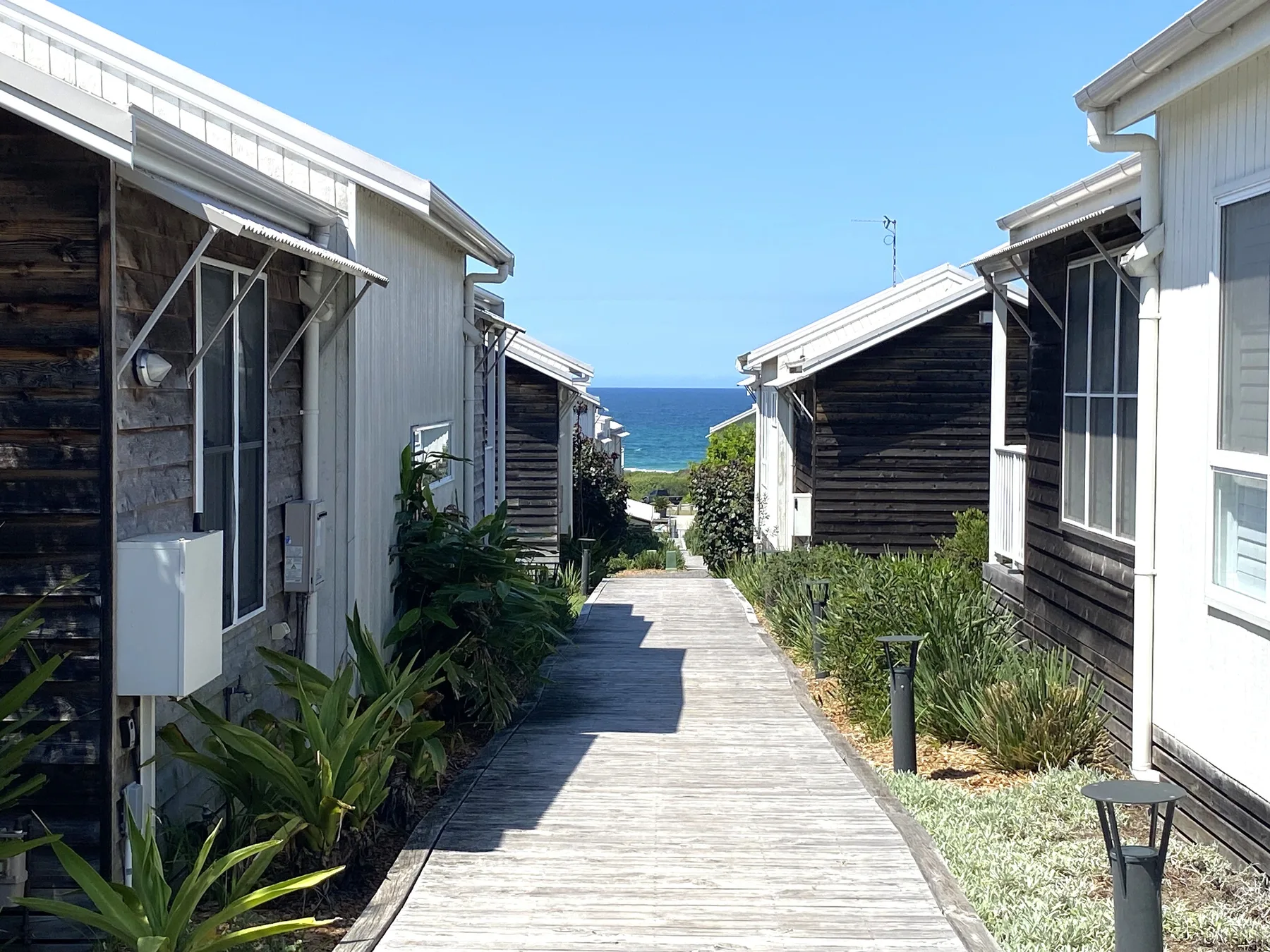 A wooden walkway runs between beach houses toward the ocean.