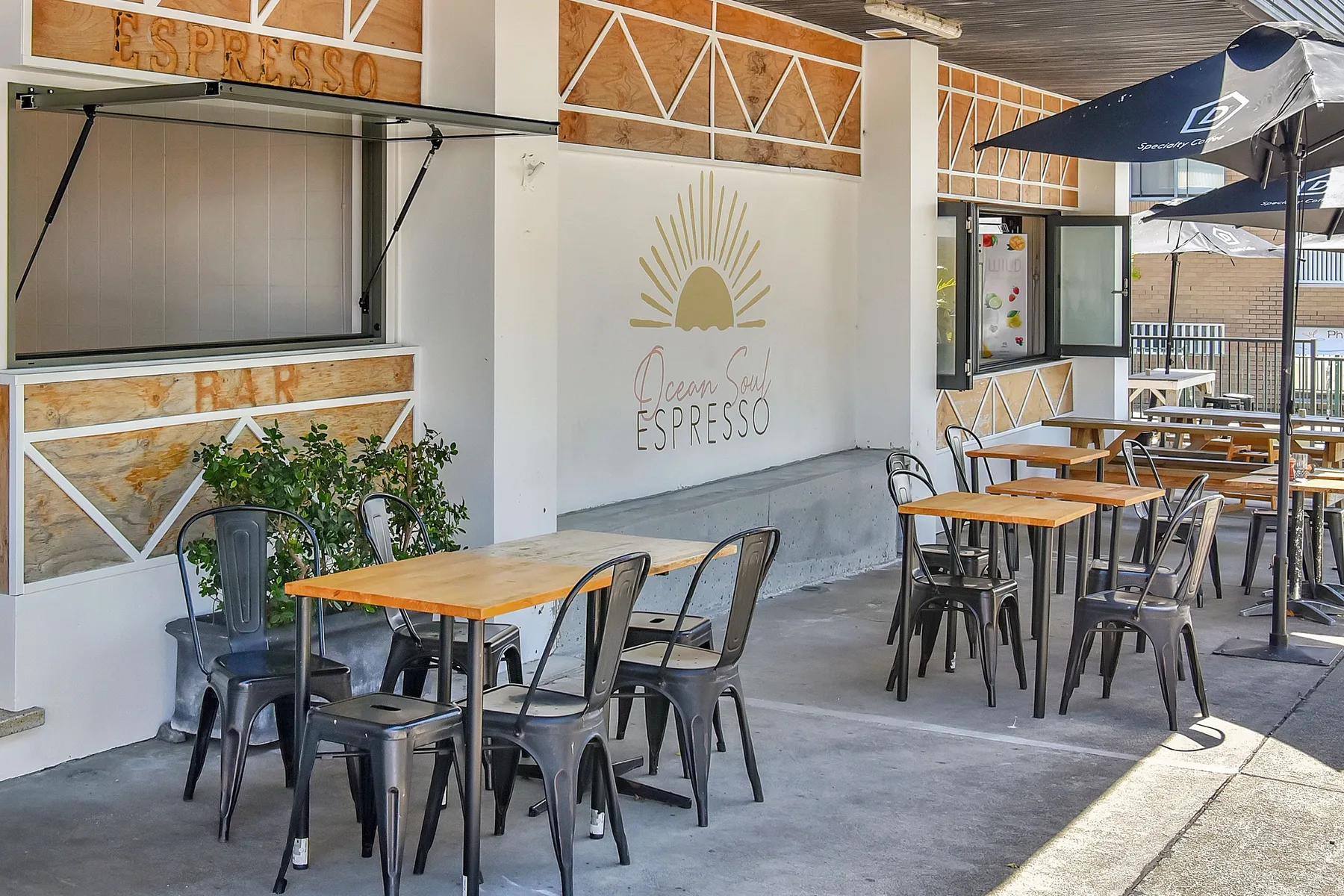 An outdoor café seating area with tables, chairs, and a wall-mounted espresso sign.