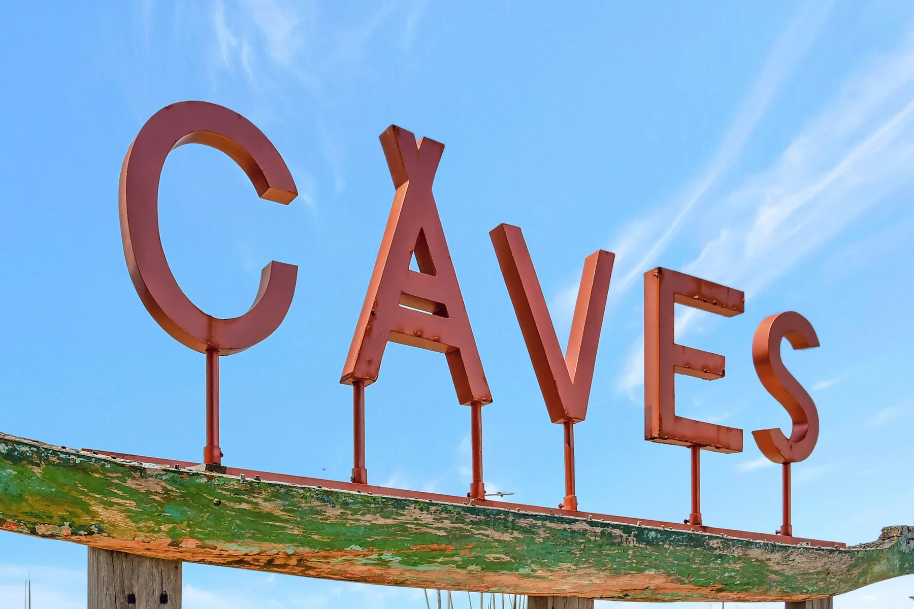 A large CAVES sign stands above a weathered green beam against the sky.