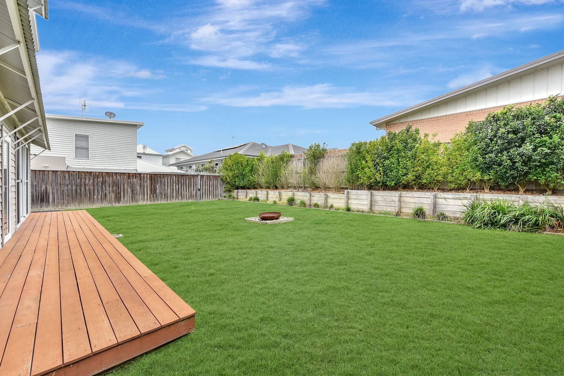 A grassy backyard with a wooden deck and garden beds along the fence.