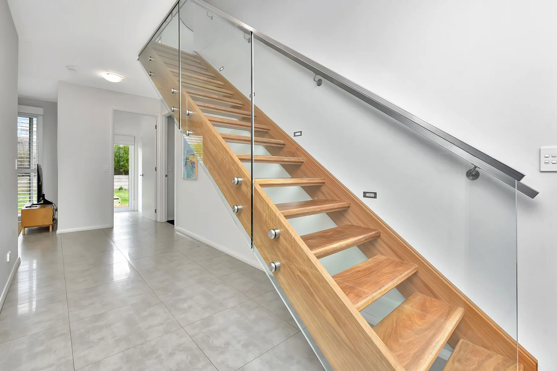 A bright hallway with a wooden staircase and glass railing.